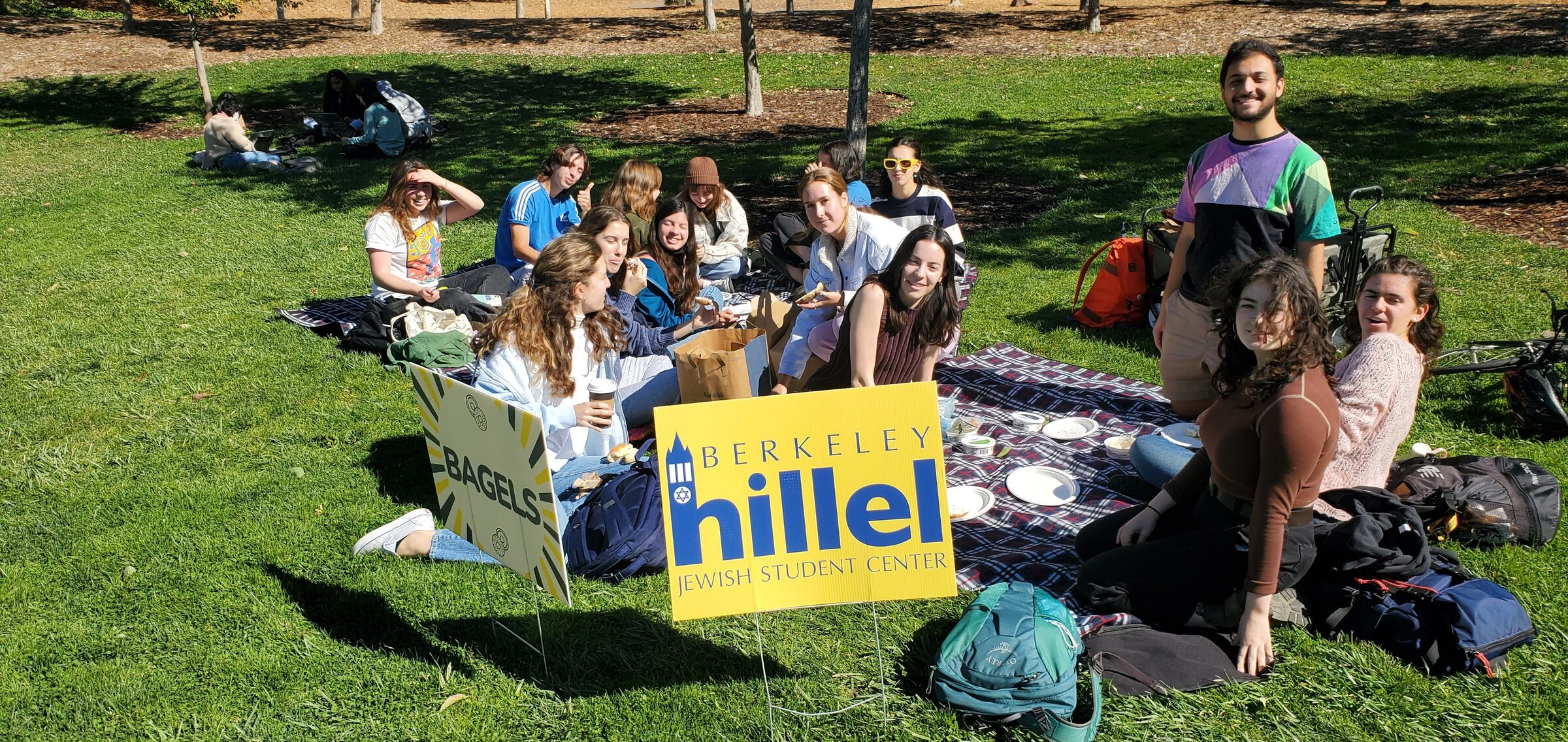 Students sitting together on a campus lawn around a Berkeley Hillel banner