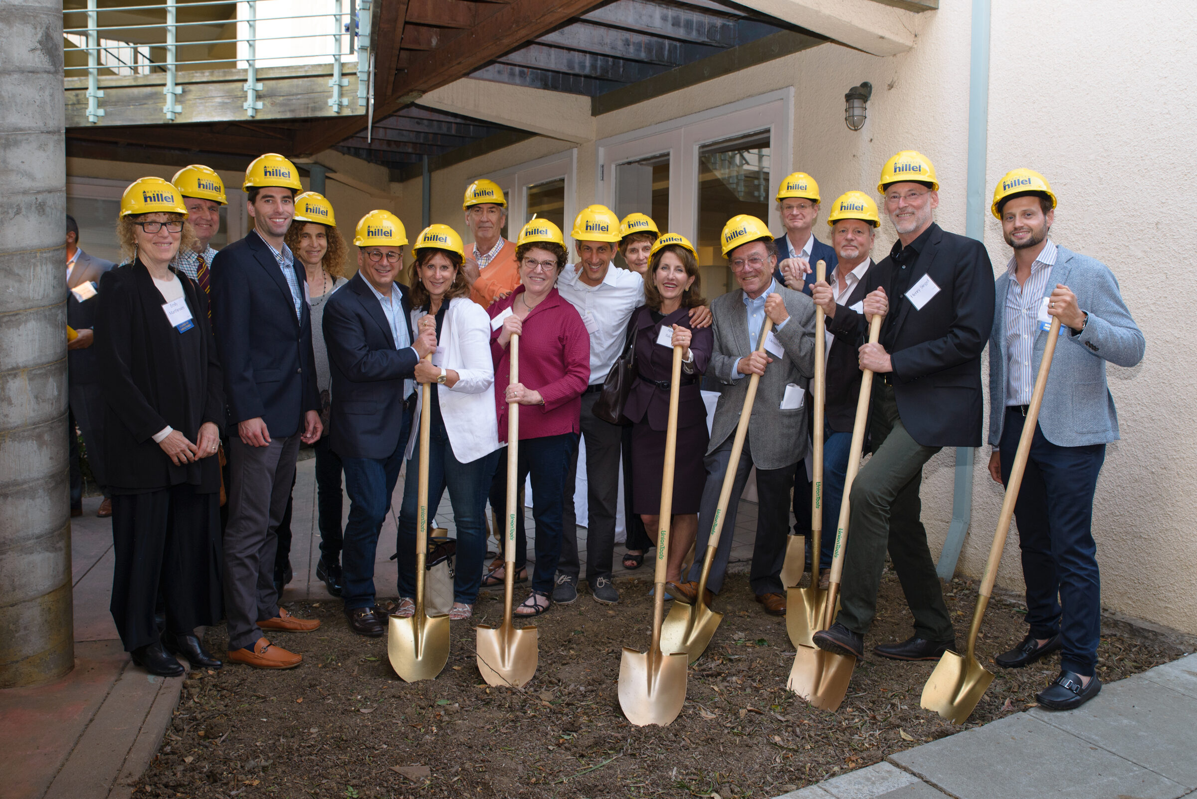 Board members in yellow hard hats holding ceremonial gold shovels at a groundbreaking