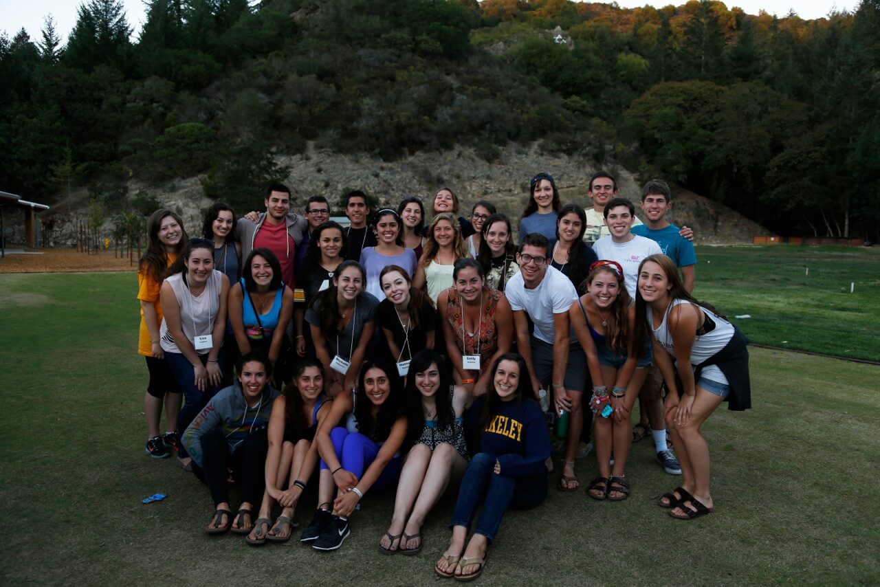 A large group of students posed together on a lawn below a hillside