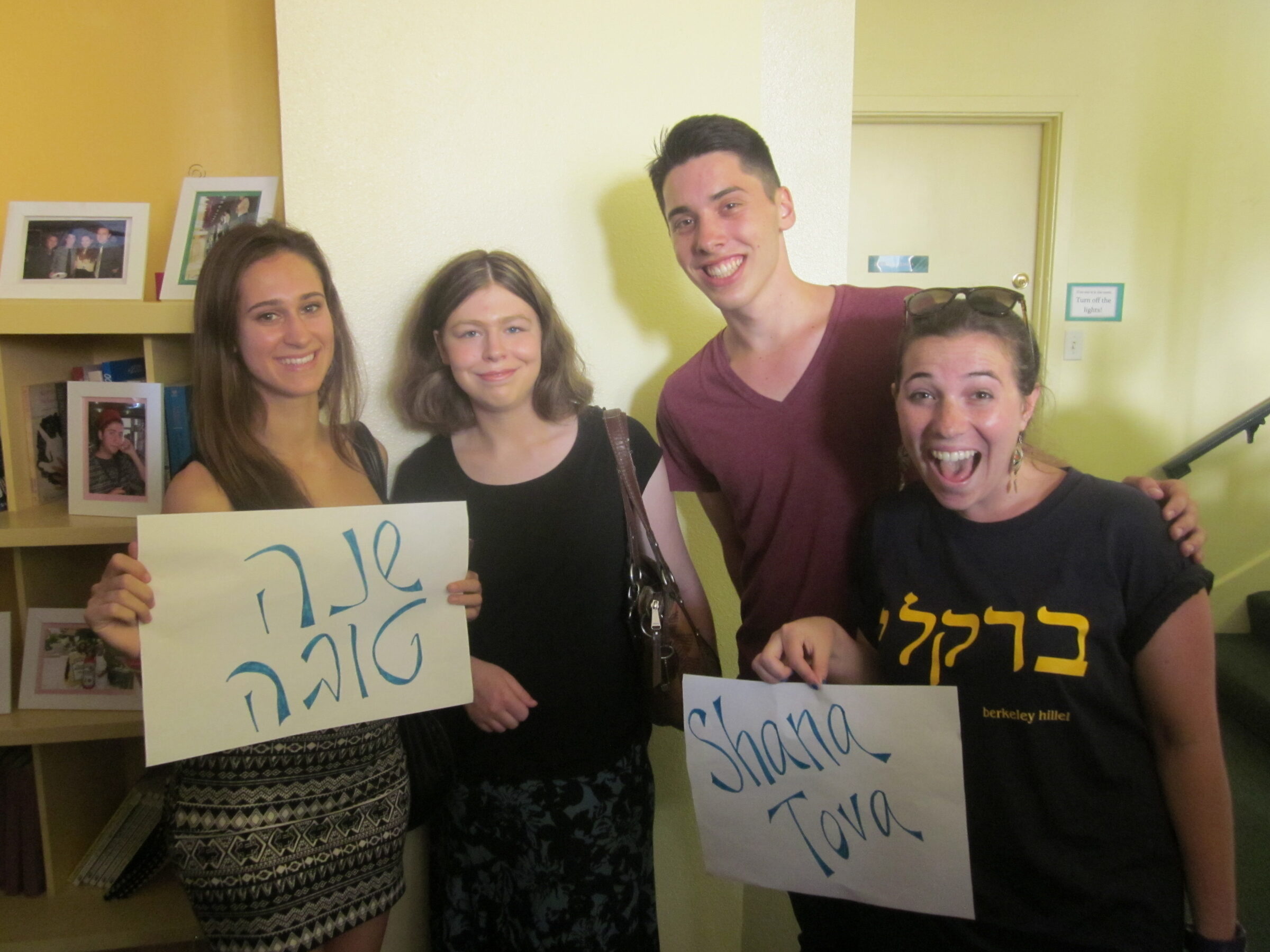 Four students holding hand-made signs reading “Shana Tova” in Hebrew and English